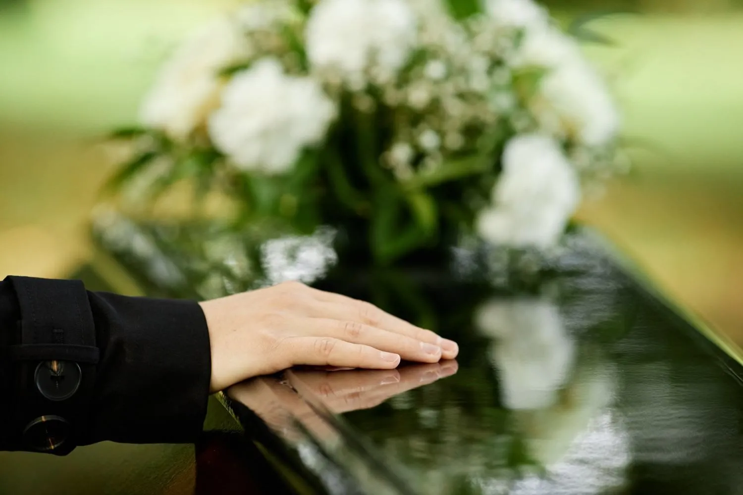Hand resting on a casket beside white flowers
